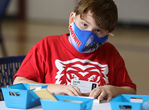 A boy wearing a face mask and sitting at a table.